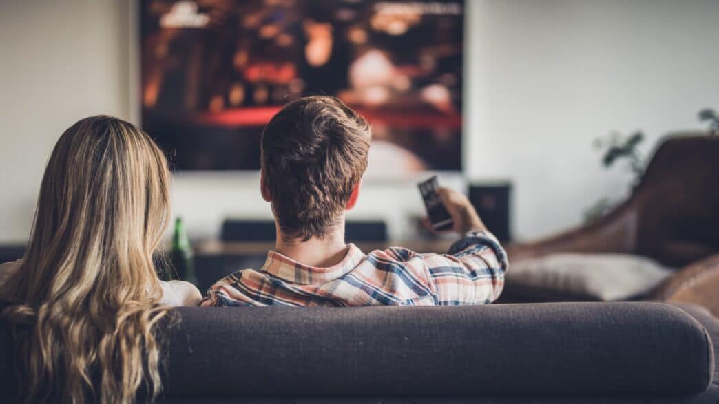rear-view-of-a-couple-watching-tv-while-relaxing-on-the-sofa-at-home-picture-id1132715308-1044×587