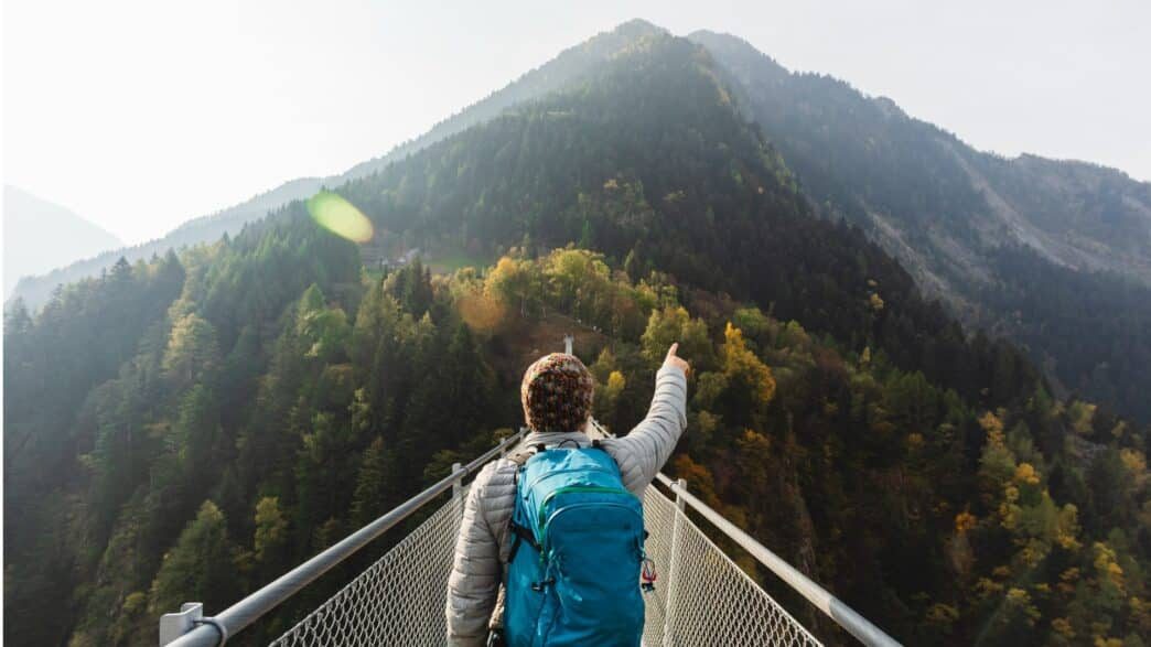 solo-hiker-pointing-with-hand-on-suspension-bridge-picture-id1055872516-1044×587
