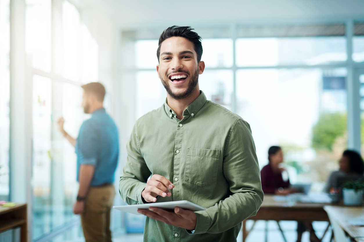Portrait of a young businessman using a digital tablet in an office with his colleagues in the background
